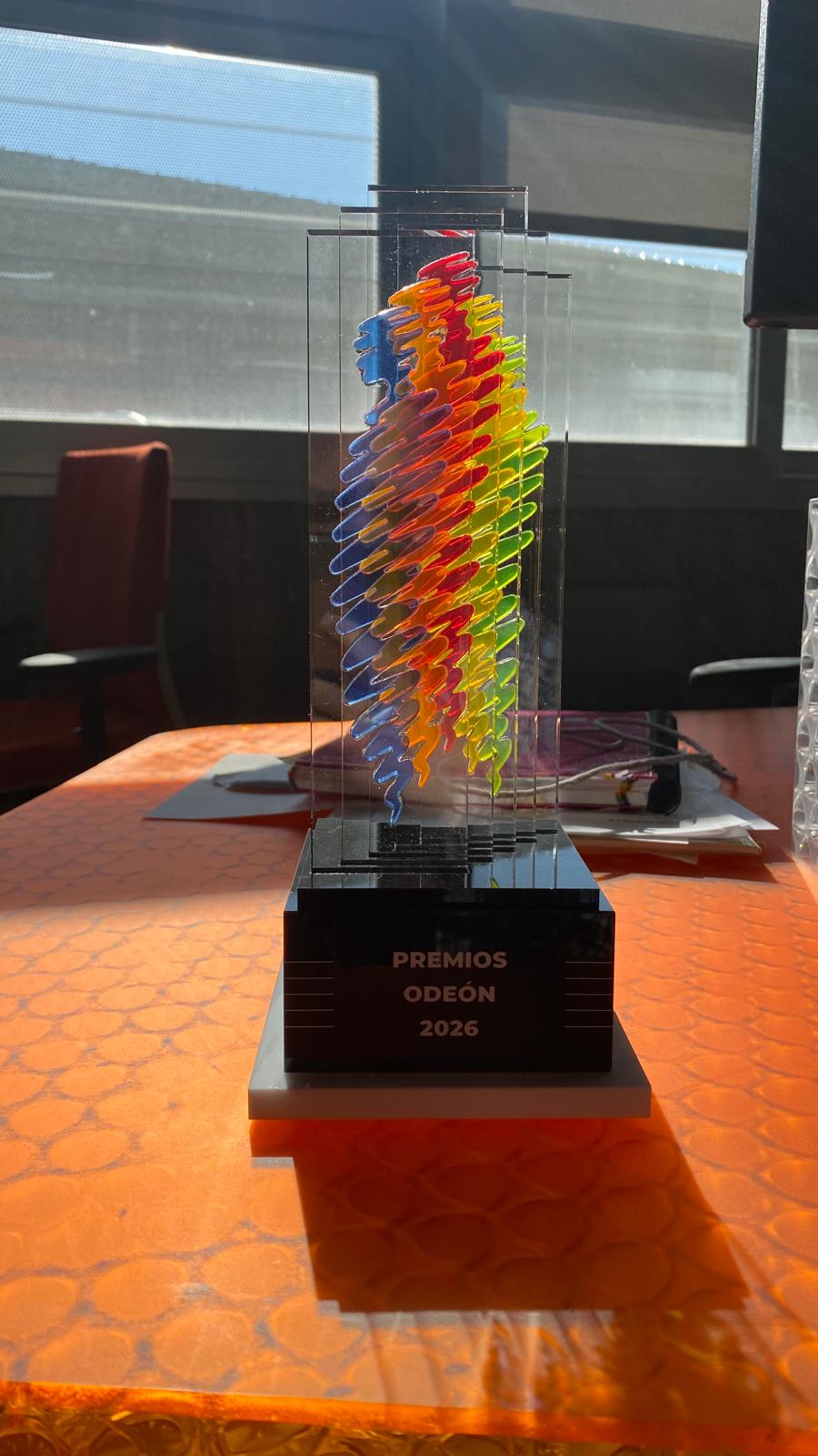 Pieza de capas transparentes y elementos de colores sobre una base con la inscripción Premios Odeón 2026